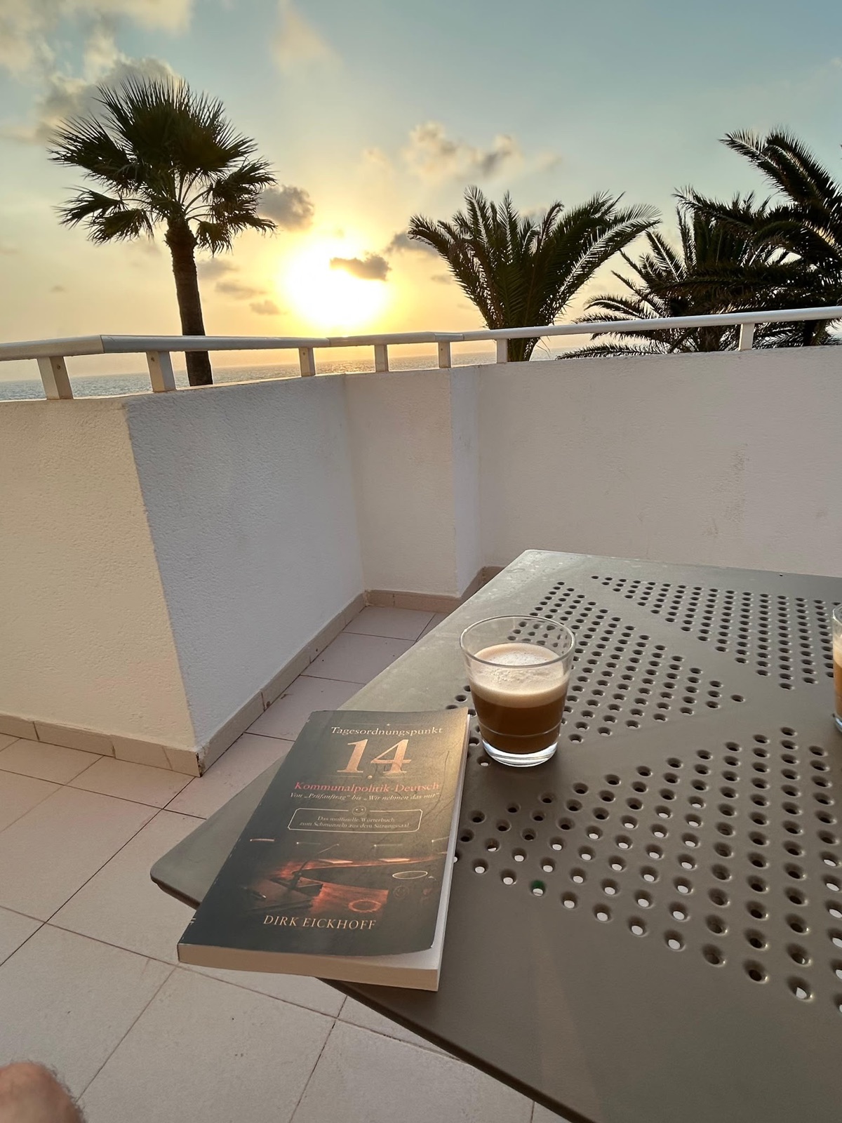 Das Buch „Tagesordnungspunkt 14“ auf einem Balkontisch bei Sonnenuntergang unter Palmen